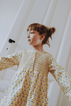 Enfant portant la robe ALMA coupe longue à manches longues boutonnée sur le devant couleur beige motif fleurs jaunes en coton bio certifié GOTS style vintage