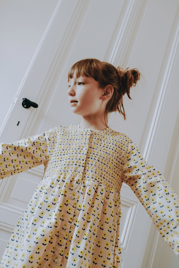 Enfant portant la robe ALMA coupe longue à manches longues boutonnée sur le devant couleur beige motif fleurs jaunes en coton bio certifié GOTS style vintage