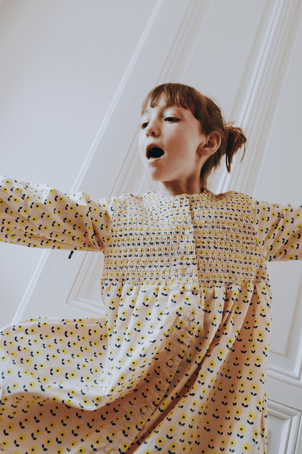 Enfant portant la robe ALMA coupe longue à manches longues boutonnée sur le devant couleur beige motif fleurs jaunes en coton bio certifié GOTS style vintage