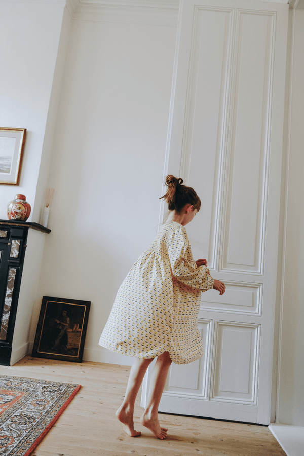 Enfant portant la robe ALMA coupe longue à manches longues boutonnée sur le devant couleur beige motif fleurs jaunes en coton bio certifié GOTS style vintage