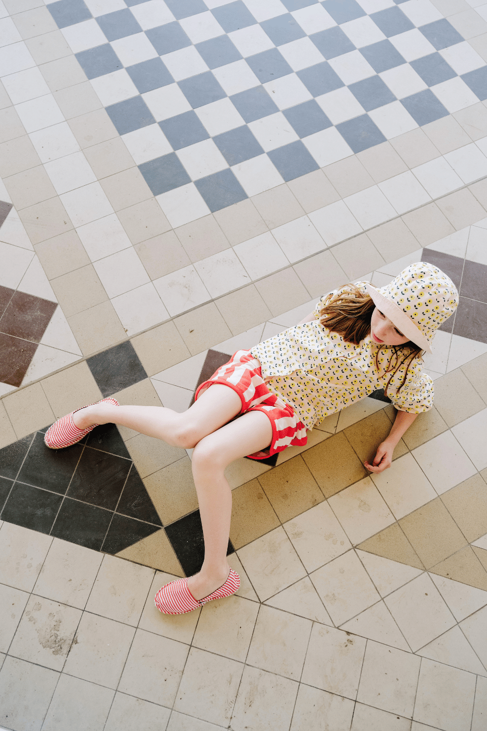 Fille portant le BOB à imprimé fleurs jaunes, la chemise SASHA à manches longues imprimé fleurs jaunes et le short KIM à rayures rouges, en coton bio style vintage mixte et unisexe