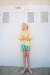 Fille portant la blouse PIA motif citron et le short KIM à rayures vertes à la plage, en coton bio style vintage mixte unisexe