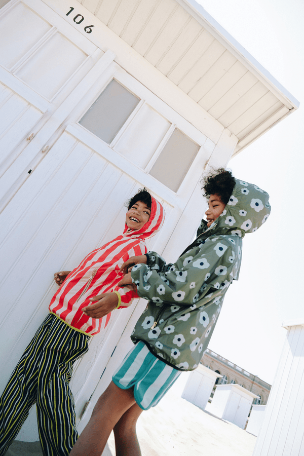 Deux enfant portant le coupe-vent REMY à motif grandes fleurs vertes et le short KIM à rayures vertes, ainsi que le coupe-vent REMY à rayures rouges, vêtements en coton bio certifié GOTS style vintage mixte unisexe