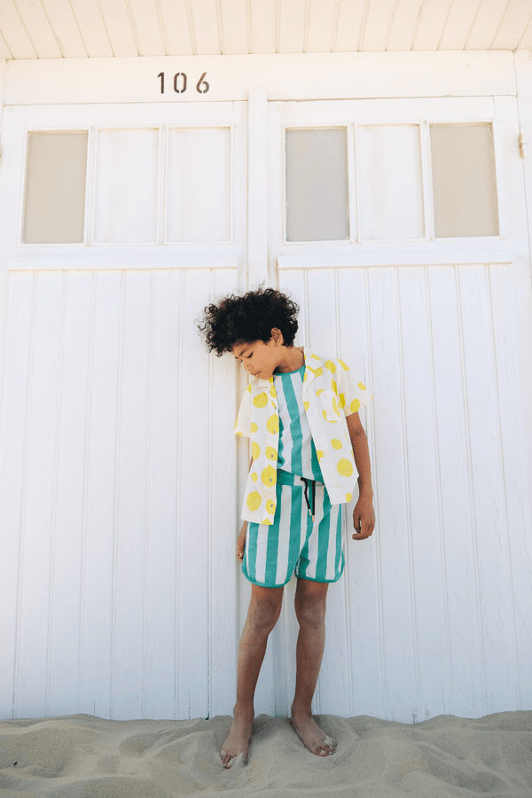 Garçon portant la chemise ARI motif citron avec le débardeur MARCEL à rayures vertes et le short KIM à rayures vertes assorti, vêtements en coton bio certifié GOTS style vintage mixte unisexe