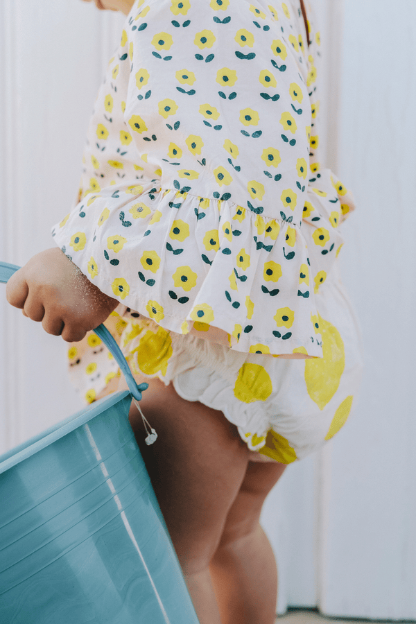 Bébé portant la blouse PIA imprimé petites fleurs jaunes et le bloomer BETTY motif citron, vêtements bébé en coton bio certifié GOTS style vintage mixte unisexe