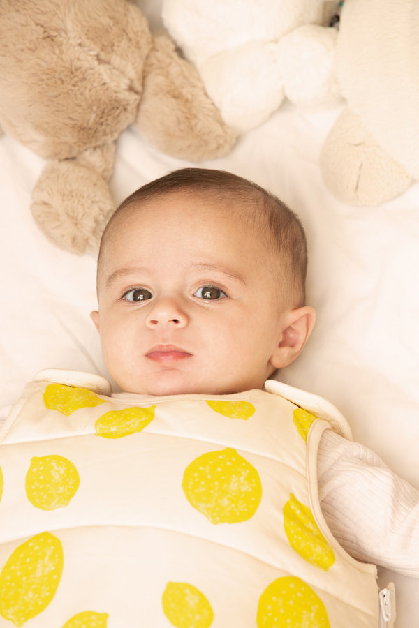 Bébé dans un lit couvert par la gigoteuse Lemon de la capsule bébé naissance en coton bio Baby Care.